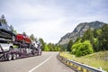 Car hauler white big rig semi truck transporting trucks on the two level hydraulic semi trailer driving on the highway road in Royalty Free Stock Photo