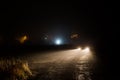 car headlight cones in night fog at field behind city