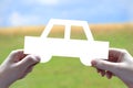 Human hands holding car shape, sky and grass in background