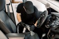 Car interior detailing concept. Young man in black t-shirt and cap, doing chemical cleaning of gray leather seats with