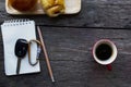 Car key on notepad with pencil and red coffee cup and bun bread on wood table backgrounds above