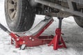 Car lifted on hydraulic Jack and Jack stand. Trolley Jack Car Lift for changing car wheels. Snowy background, falling snow