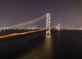 Car lights blur over Akashi Bridge with distant city at night