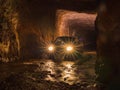 Car lights and flare inside deep old mining tunnel cave with reflection. rock wall cave with water lodge rocky road. adventure Royalty Free Stock Photo