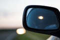 Car lights reflecting in the side mirror of a car parked on the curb of a highway