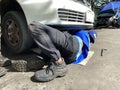 Car mechanic doing under chassis repair lying down on the pavement.