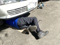 Car mechanic doing under chassis repair lying down on the pavement.