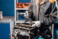 Car mechanic holding a new piston for the engine, overhaul.. Engine on a repair stand with piston and connecting rod of