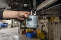 Car mechanic holding a used fuel filter in the background, car on a lift in a car workshop.