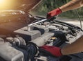 Car mechanic repairing auto engine with wrench and hood up on road