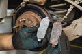 The car mechanic shows for comparison a worn brake shoe and a new one against the background of an automobile brake disc