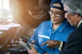 Car mechanic talking with service station manager about car maintenance list show in service tablet Royalty Free Stock Photo