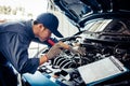 Car mechanic technician holding flashlight checking engine with checklist clipboard to maintenance vehicle by customer claim order