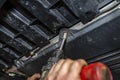 A car mechanic unscrews the bottom plastic engine cover with an electric screwdriver.