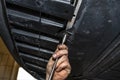 The car mechanic unscrews the bottom plastic engine cover using a socket wrench.