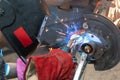 A car mechanic wearing a welding mask welds a wheel bolt to a car hub