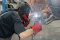 A car mechanic in a welding mask welds broken off wheel bolts to the car hub. selective focus