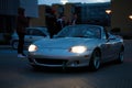 Car meet Mazda Miata MX-5 MB with headlights on arriving in the evening