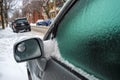 Car mirror and windows are covered with ice after freezing rain.