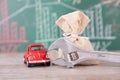 Car model and money bag in front of financial blackboard and a pair of pliers holding dollar coins