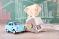 Car model and money bag in front of financial blackboard and a pair of pliers holding euro coins