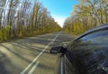 The car moves along a straight asphalt country road. On the edges of the roadside there are autumn trees. In the Royalty Free Stock Photo