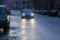 Car is moving slowly and carefully on rainy autumn day. Headlights are on. Other cars are parked at road side. Motion blur Royalty Free Stock Photo