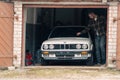 A car owner looking on his white classic convertible BMW E30 car in the opened garage.