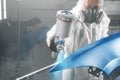 Car paint worker spraying blue paint to car body element using spray gun in vehicle workshop chamber. Complex Royalty Free Stock Photo