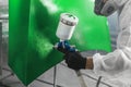 Car paint worker spraying green paint to car body element using spray gun in vehicle workshop chamber. Complex Royalty Free Stock Photo