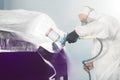 Car paint worker spraying purple paint to car body element using spray gun in vehicle workshop chamber. Complex Royalty Free Stock Photo