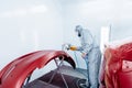 Car painter in protective clothes and mask painting automobile bumper with red paint and varnish in chamber workshop. Royalty Free Stock Photo