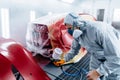 Car painter in protective clothes and mask painting automobile bumper with red paint and varnish in chamber workshop. Royalty Free Stock Photo