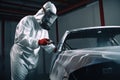 Car painter in protective clothes paints automobile with paint in chamber workshop. Generative AI Royalty Free Stock Photo