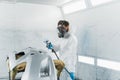 Car painter in a protective suit and mask varnishes a painted bumper of a vehicle while working in a painting booth. Royalty Free Stock Photo