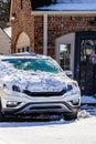 Car parked in driveway of brick house with windshield partly covered with snow