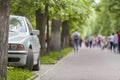 Car parked in pedestrian zone under trees along street with walking people on summer day Royalty Free Stock Photo