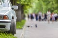 Car parked in pedestrian zone under trees along street with walking people on summer day Royalty Free Stock Photo