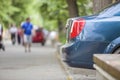 Car parked in pedestrian zone under trees on city street with walking people on summer day Royalty Free Stock Photo