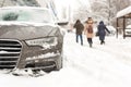 Car parked in snowdrift at city street. Heavy winter snowfall . People walking while strong snow and wind. Storm blizzard