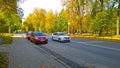 Car parking and driving on city road. Yellow dry fallen leaves on asphalt. Golden autumn street. Fall. Tree. Green orange town.