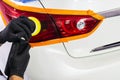 Car polish wax worker hands applying protective tape on the rear lights before polishing. Buffing and polishing car headlight. Car