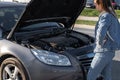 Car problem. Driver girl near open hood auto after accident triangle on road. Vehicle broken down or motor car engine Royalty Free Stock Photo