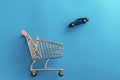 Car purchase concept. Toy blue automobile falling to shopping trolley cart on blue background. Buying new car. Online