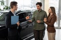 Car purchase or lease concept. Cheerful young couple taking car key from auto salesman at modern dealership Royalty Free Stock Photo