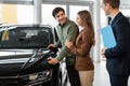 Car purchase or rental. Millennial Caucasian couple speaking to salesman about buying new automobile at dealership Royalty Free Stock Photo