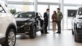 Car purchase or rental. Positive young spouses speaking to salesman about buying new auto at dealership, panorama Royalty Free Stock Photo