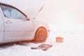 A car with a raised hood on a background of a snowy field, tools and a discharged car battery near the car, the concept of a car