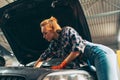 Car reapir. Young red-headed girl, auto mechanic working at auto service station using different work tools. Gender Royalty Free Stock Photo