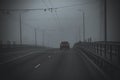 Car with red tail lights driving on a bridge in a very foggy and dark weather